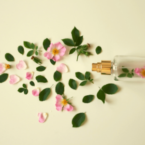 A flatlay of leaves and pink flowers surrounding a clear spray bottle containing pink flowers.