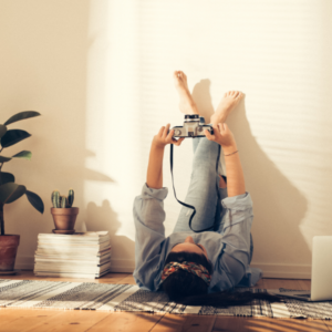 Person lying on their back on the floor with their legs up the wall, holding a camera.