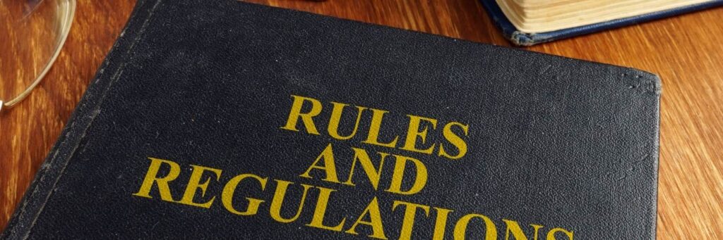 A black leather book on a wooden table. The book is titled Rules and Regulations.