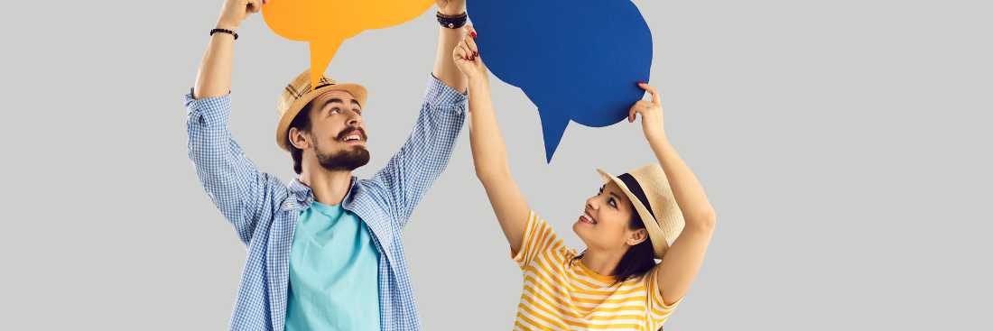 Two people wearing hats & holding paper speech bubbles. They are smiling and looking above their heads at the speech bubbles.