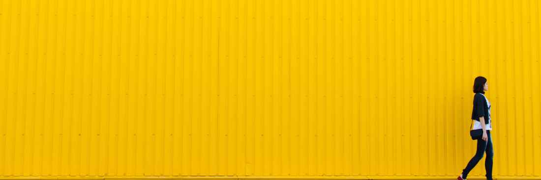 A person walking in front of a yellow wall.