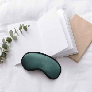 A photo of an open book with a blindfold and a sprig of silverdollar eucalyptus beside it on a bed.