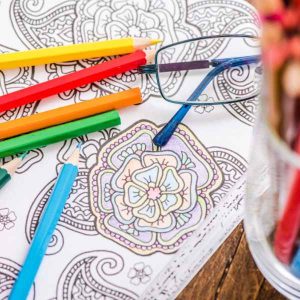 A colouring book with some coloured pencils and glasses on top.