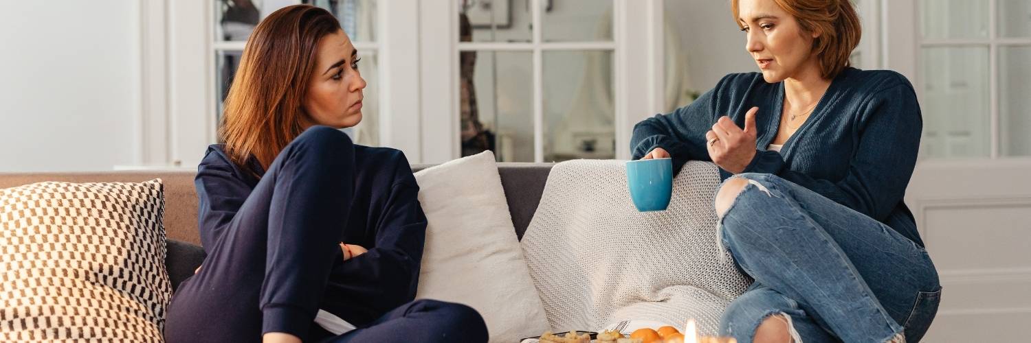 Two women on a lounge talking to each other.