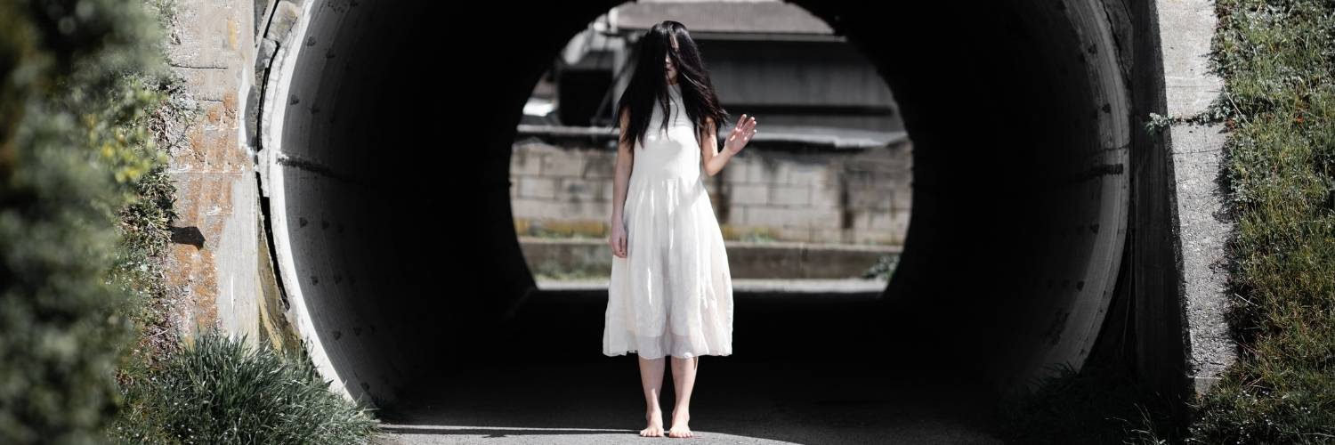A woman in a white dress in front of a large circular pipe.